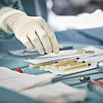 Close shot of a surgeon's gloved hand reaching for syringes on table.