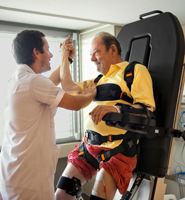 An elderly man is doing exercise with the help of a care taker